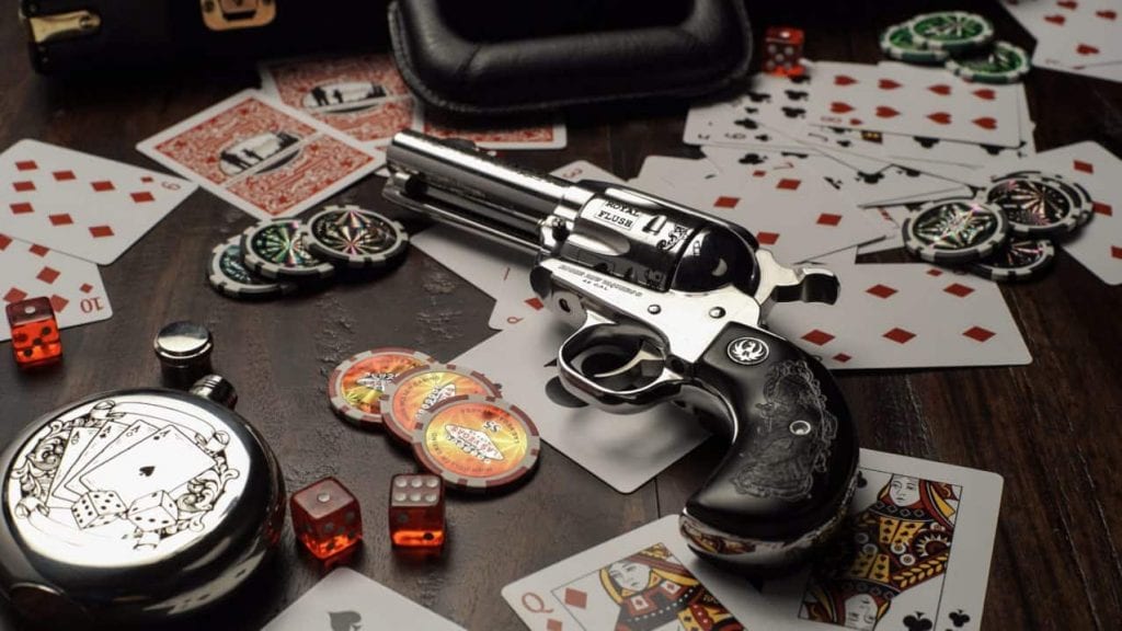 a gun next to casino chips and cards on a wooden table 