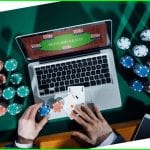 a man playing poker on his laptop with poker chips next to him